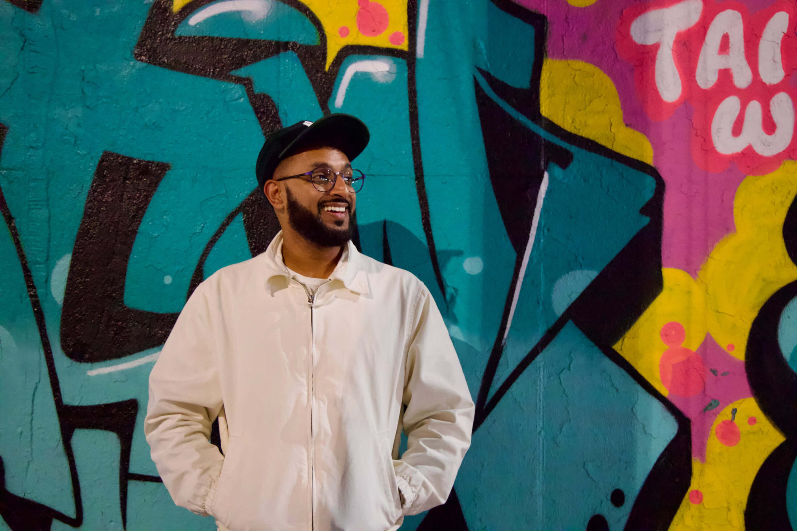 Brooklyn comedian Ali Sultan smiles in front of funky street art in Bushwick, NY.